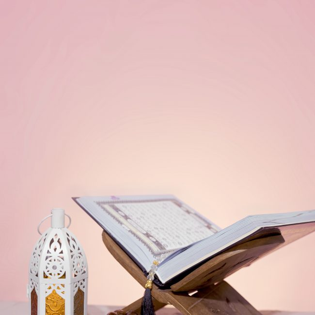Quran open in wooden placemat. Holy month in the Muslim world - Ramadan Kareem. Eid-al-adha concept. Wooden Rehal with open holy book Quran and rosary beads. Arabic lantern colorful spring flowers